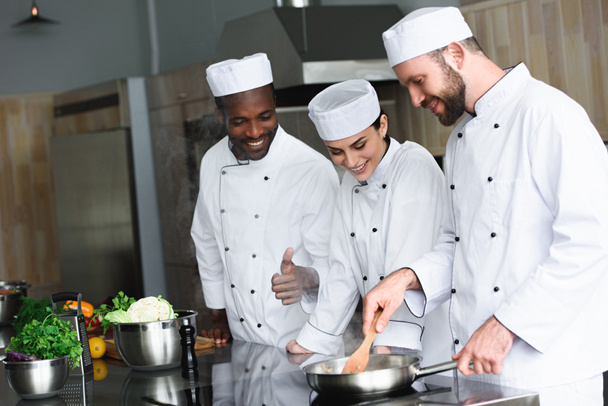мультикультурні кухарі смажать овочі на сковороді на кухні ресторану
 - Фото, зображення