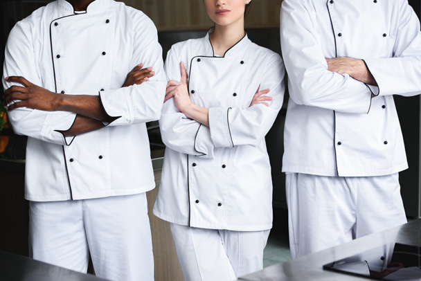 imagen recortada de chefs multiculturales de pie con los brazos cruzados en la cocina del restaurante
 - Foto, Imagen