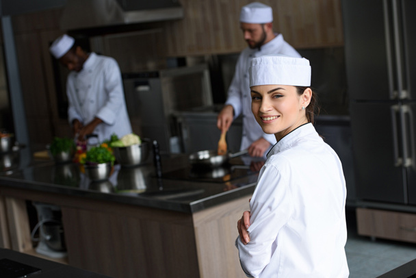 smiling beautiful chef looking at camera at restaurant kitchen - 写真・画像
