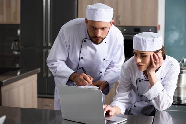 chefs masculinos y femeninos usando laptop en la cocina del restaurante
 - Foto, Imagen