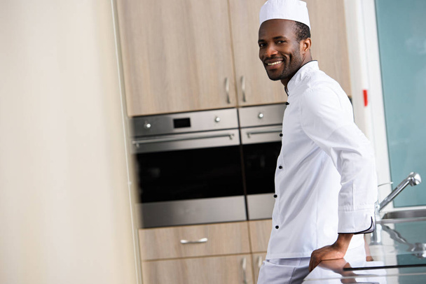 side view of handsome african american chef leaning on kitchen counter at restaurant kitchen - Photo, Image