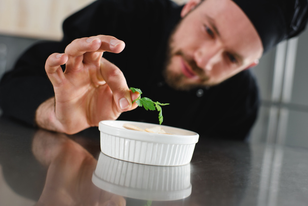 guapo chef añadiendo perejil al plato en la cocina del restaurante
 - Foto, Imagen