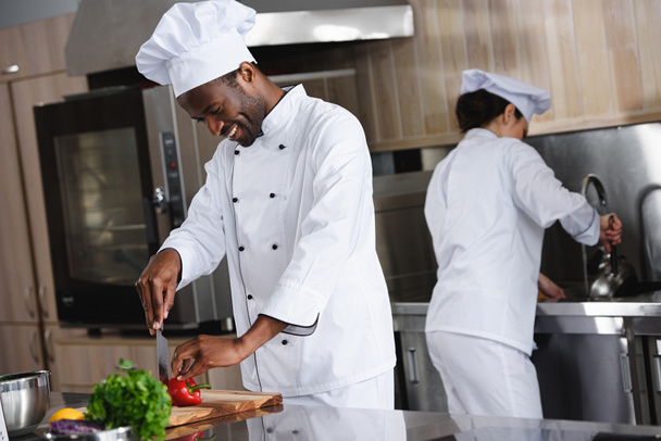 african american chef cutting bell pepper at restaurant kitchen - Foto, Imagen