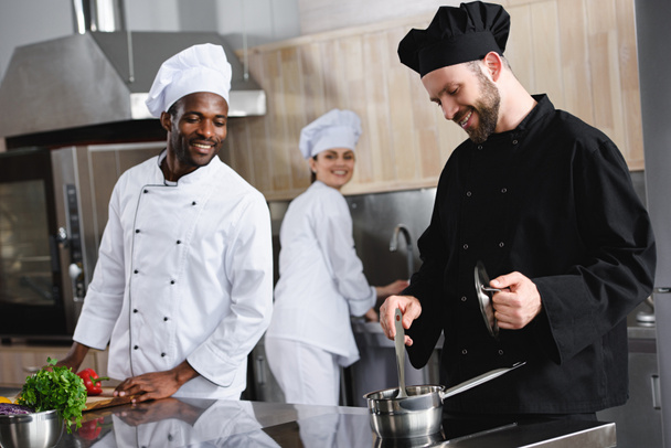 chefs multiculturales sonrientes cocinando juntos en la cocina del restaurante
 - Foto, imagen