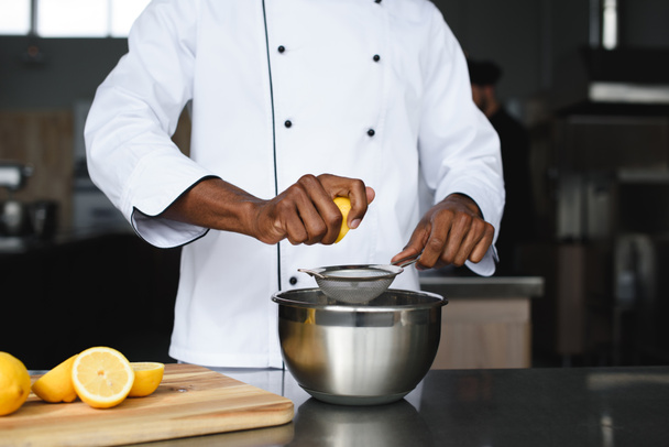περικομμένη εικόνα του Αφρικανός Αμερικανός σεφ σφίγγετε τα λεμόνια σε κουζίνα εστιατορίου - Φωτογραφία, εικόνα