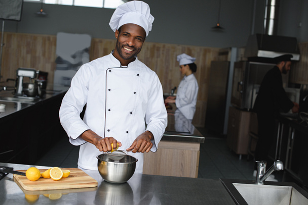 sonriente guapo africano americano chef exprimiendo limones en restaurante cocina
 - Foto, Imagen