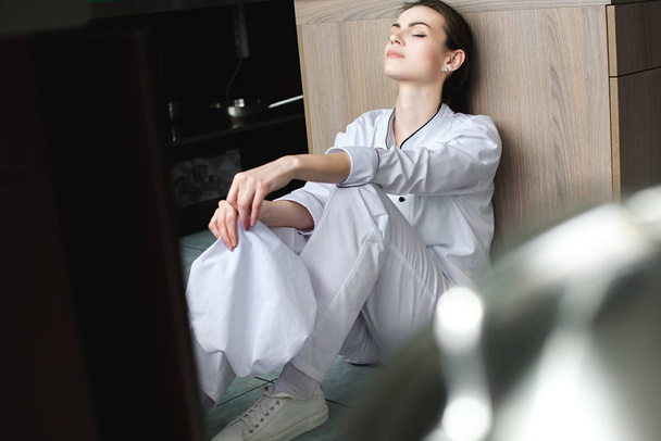 attractive tired chef sitting with closed eyes on floor at restaurant kitchen - Photo, Image