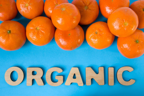 Naturalne mandarynki leżą w stosach na siebie na niebieskim tle z napisem organic z trójwymiarowe litery. Pojęcie naturalne bez Gmo żywności i suplementów diety i owoców - Zdjęcie, obraz