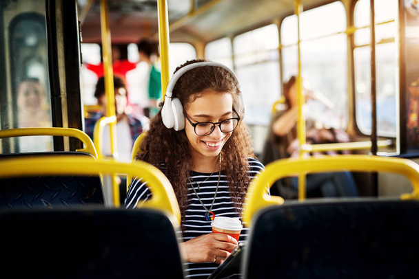 音楽を聴くと、コーヒーを飲みながらバスの座席に座っている若いかわいい女性  - 写真・画像