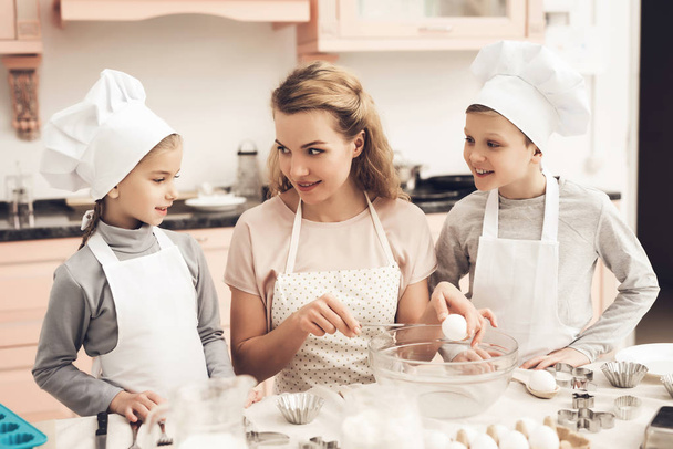 Madre enseñando a sus hijos con sombreros blancos preparando galletas en la cocina
 - Foto, imagen