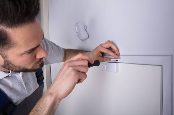 Junge männliche Techniker installieren Sicherheitssystem Türsensor an Wand mit Schraubenzieher - Foto, Bild