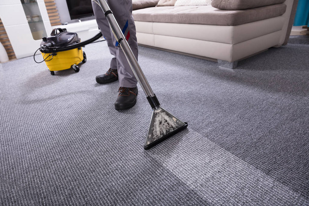 Low Section Of A Person Cleaning The Carpet With Vacuum Cleaner In Living Room - Foto, Imagen