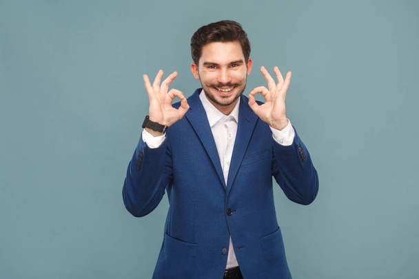 handsome businessman with mustache showing ok signs at camera on light blue background, concept of richly and success business people  - Foto, Imagen