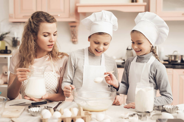 Mother teaching her children in white hats preparing cookies at kitchen - Foto, afbeelding