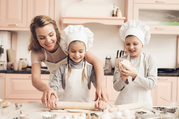 Enfants dans des chapeaux blancs et mère faire des biscuits à partir de pâte à la cuisine
 - Photo, image