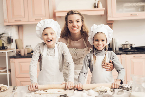 Children in white hats and mother making cookies out of dough at kitchen - Фото, зображення