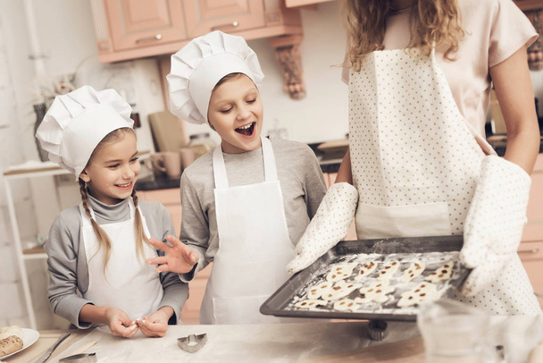 Children in white hats at kitchen and mother holding tray with cookies - Foto, Imagen