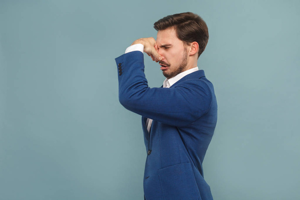 unhappy man with closed nose hand showing bad smell sign on light blue background, concept of richly and success business people  - Fotoğraf, Görsel
