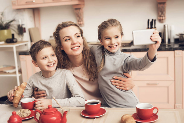 Children with mother drinking tea and taking selfie on smartphone - Фото, изображение