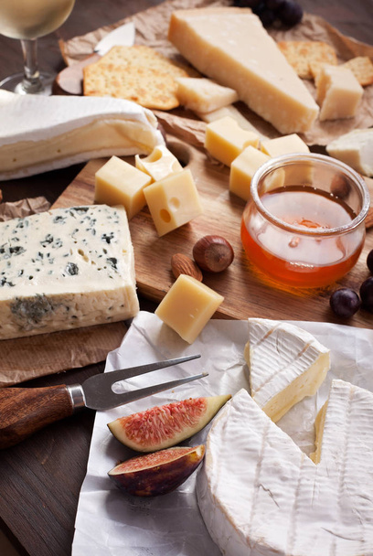 Variety of different cheese with wine, fruits and nuts. Camembert, goat cheese, roquefort, gorgonzolla, gauda, parmesan, emmental - Photo, Image