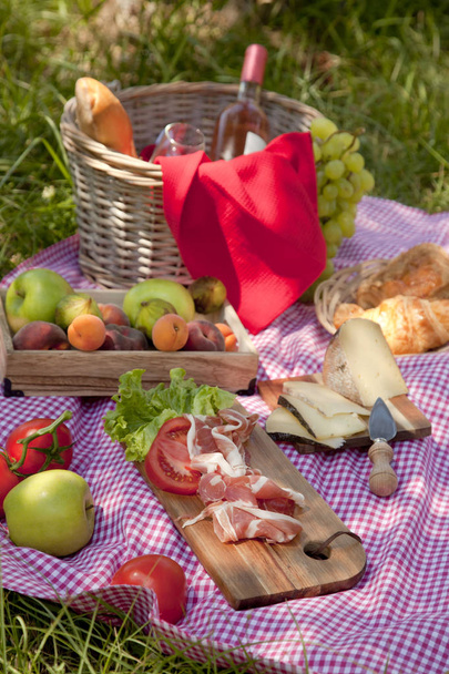 Пикник в парке на траве: скатерть, корзина, здоровое питание, розовое вино и аксессуары
 - Фото, изображение