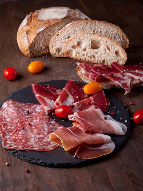 Fleischvorspeisen - Wurst, Schinken, Speck mit frischem Brot und Tomaten - Foto, Bild