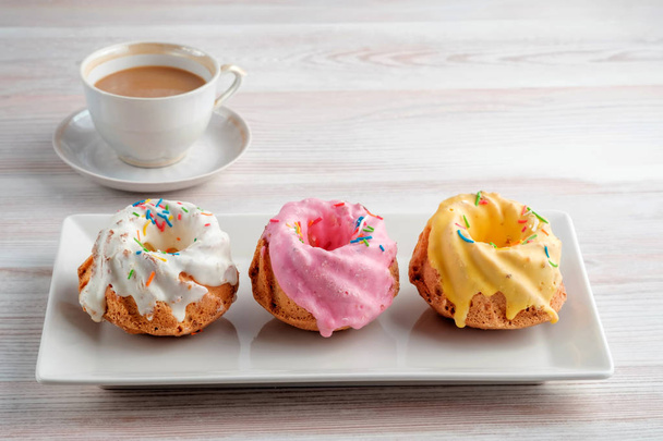 Tre cupcake multicolori su un piatto rettangolare e una tazza di espresso su una texture leggera del tavolo. Copia lo spazio del testo
. - Foto, immagini