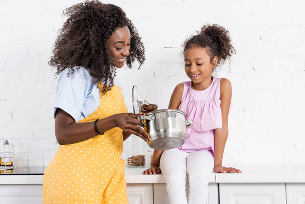 Gelukkig Afro-Amerikaanse moeder en dochter samen koken op keuken - Foto, afbeelding