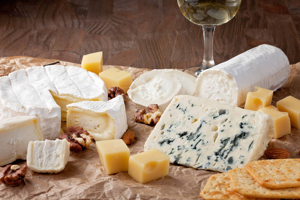 Variety of different cheese with wine, fruits and nuts. Camembert, goat cheese, roquefort, gorgonzolla, gauda - Photo, Image