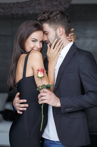 Χαρούμενος νεαρός με τριαντάφυλλο εκμετάλλευση αγκαλιάσει όμορφη γυναίκα εσωτερική - Φωτογραφία, εικόνα