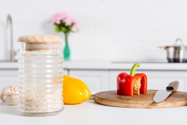 rice in glass jar and bell peppers on wooden board with knife  - Fotó, kép