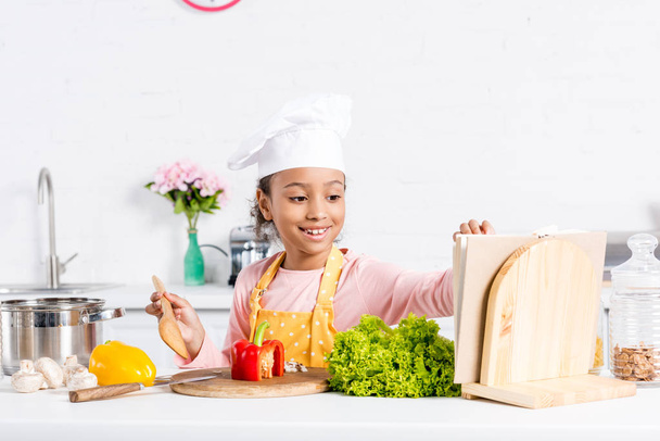allegro bambino afroamericano in grembiule e cuoco cappello cucina su cucina
 - Foto, immagini