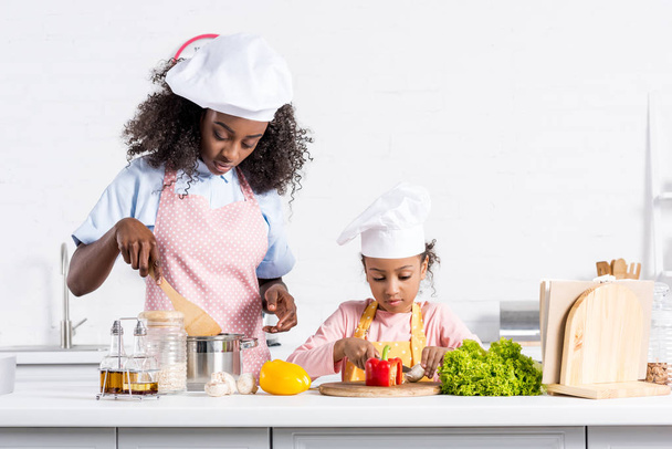 africano americano madre e hija en chef sombreros cocinar en cocina
 - Foto, Imagen
