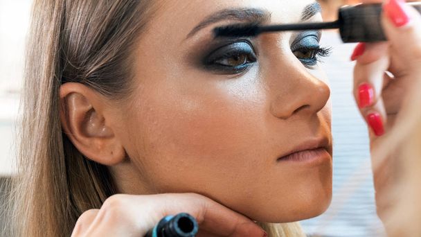 Closeup Image of Makeup artist painting young models eyes with black mascara - Photo, image