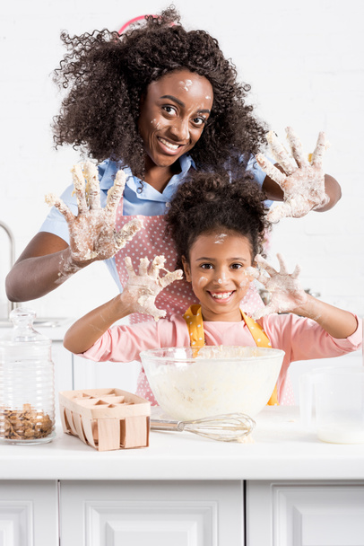 Afro-Amerikaanse moeder en grappige dochter handen tonen in deeg op keuken - Foto, afbeelding