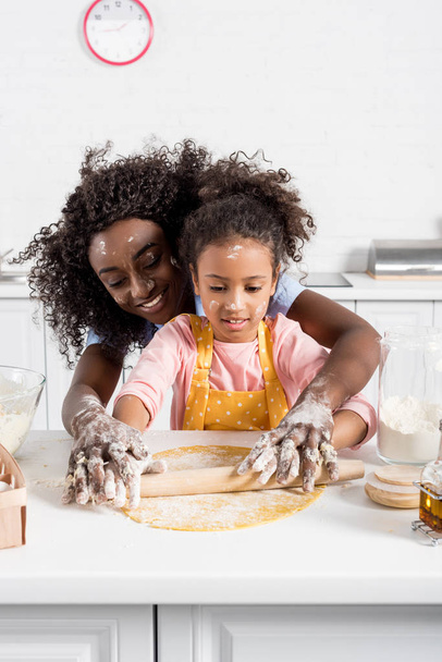 african american mother and daughter rolling dough with pin together on kitchen - 写真・画像