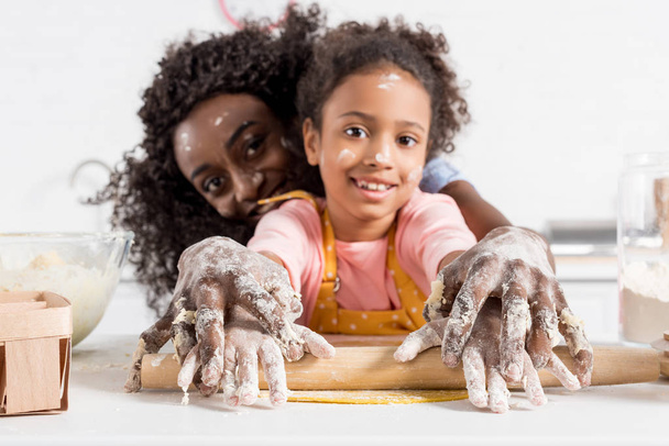 afro-américaine mère et fille souriante rouler pâte avec rouleau à pâtisserie ensemble sur la cuisine
 - Photo, image
