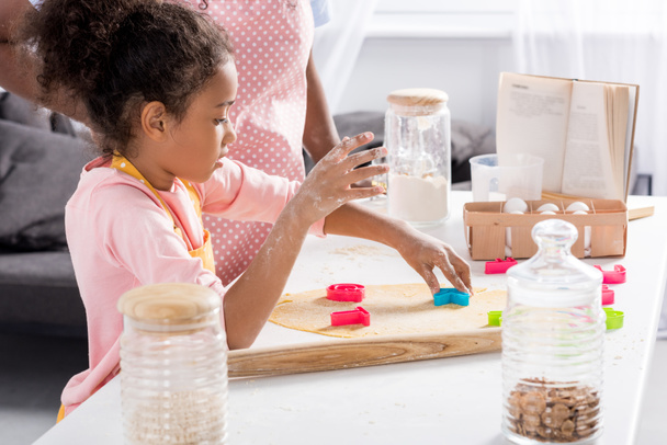 Afro-Amerikaanse dochter maken van koekjes met cookie cutters op keuken - Foto, afbeelding