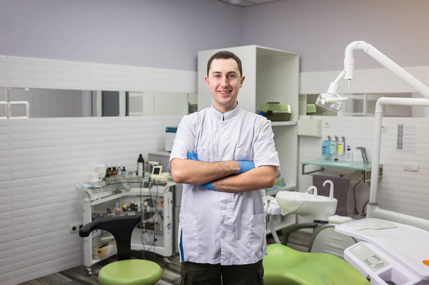 Dentysta mężczyzna stojący z jego ręce skrzyżowane na tle biura medycznego. Opieki zdrowotnej, zawodu, implantologii i medycyny pojęcie - Zdjęcie, obraz