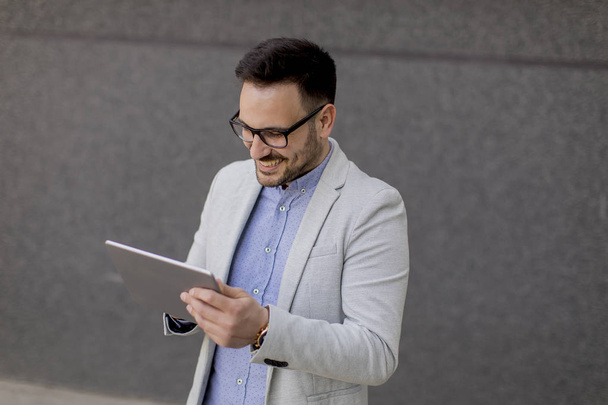 Bonito jovem empresário com tablet digital na parede cinza
 - Foto, Imagem