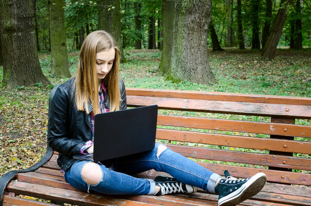 留学屋外。若い女性が公園のベンチに座ってパソコンのキーボード入力します。金髪女性 10 代の大学で彼女の講演後ネット書籍に取り組んで。コピーのテキストのための領域. - 写真・画像