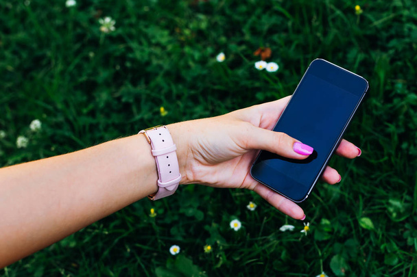 la chica sostiene el teléfono en su mano con una pantalla grande en el fondo de hierba verde
 - Foto, Imagen