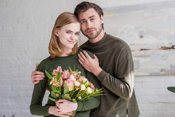 front view of stylish young woman holding flowers and boyfriend embracing her  - Photo, Image