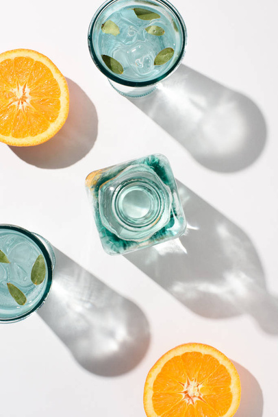 adet portakal, şişe ve bardak su ve buz beyaz yüzey üzerinde düz lay - Fotoğraf, Görsel