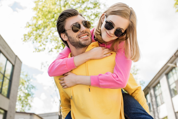 young man in sunglasses doing piggyback ride to girlfriend  - Photo, Image