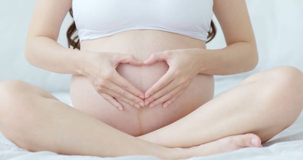 close up pregnant woman's  hands in heart shape on belly - Foto, imagen