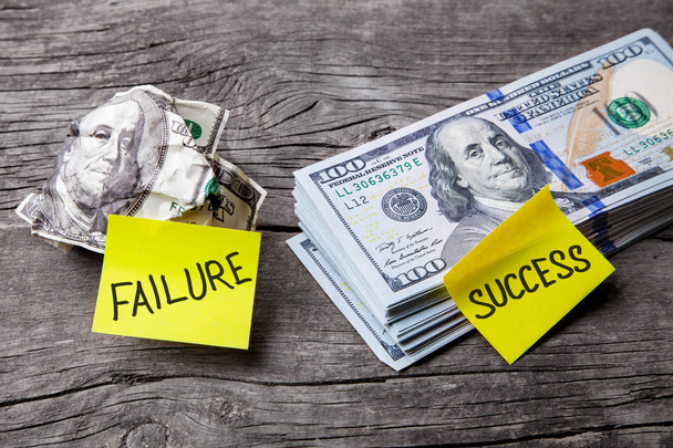 Success and failure in business, choice of ways, concept. Office stickers on dented banknote and pile of dollars. Wooden background - Фото, изображение