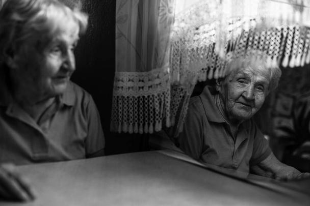 eine ältere Frau betrachtet ihr Spiegelbild in einem dunklen Raum. - Foto, Bild