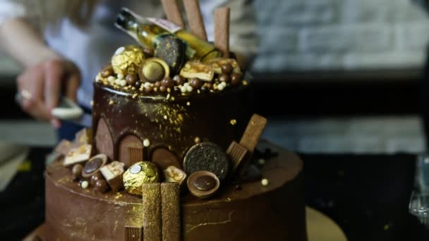 confectioner takes upper tier big fabulous chocolate cake decorated with candies and sprinkled with food gold - Footage, Video