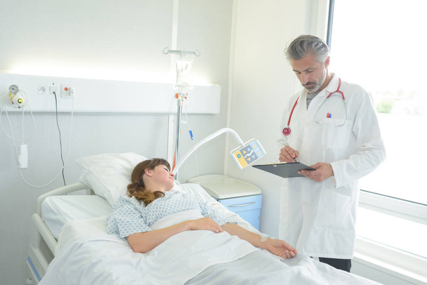 doctor with clipboard standing near patient lying on bed - Foto, immagini